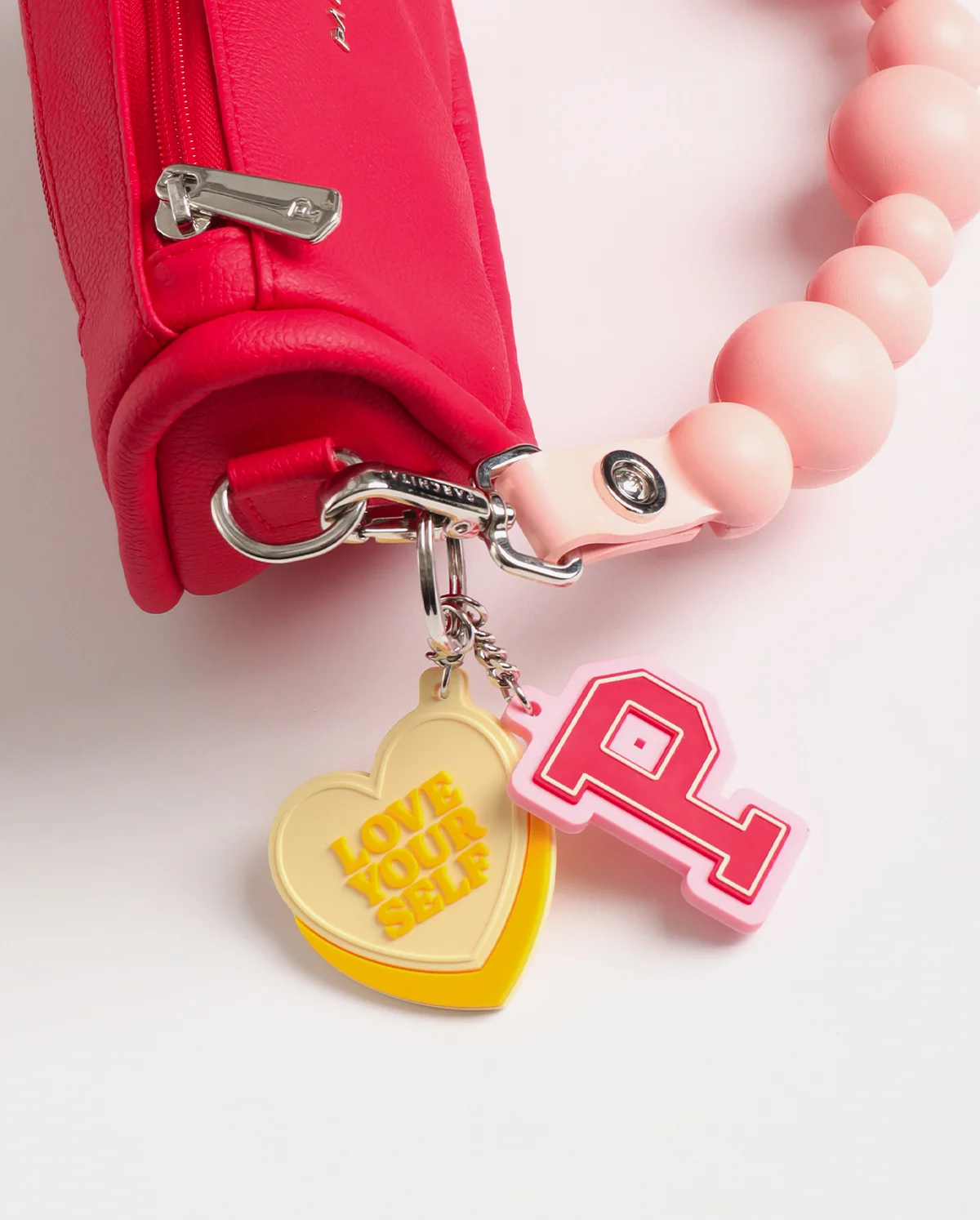Bolso Lumina Rojo - detalle de colgantes: P universitaria rosa y corazón Love Yourself amarillo